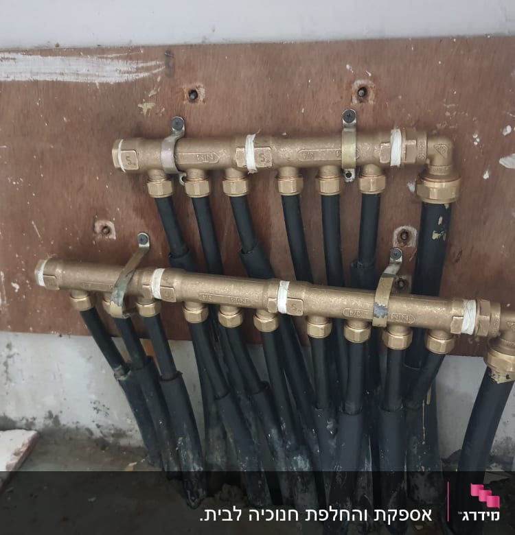 צינורות שחורים מחוברים למפצל פליז על קיר עץ